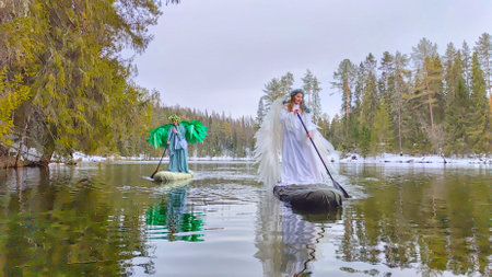 Girls in white and green dresses role-play the enchanting meeting of winter and spring on a tranquil lakeの写真素材