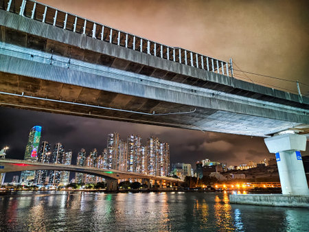The vibrant skyline of Hong Kong showcases buildings lit up against a dark sky beneath a busy bridge at night.の写真素材