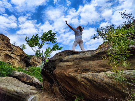 Blonde woman stands confidently on a rocky outcrop surrounded by lush greenery, reveling in nature's beauty and her blogging journey.の写真素材