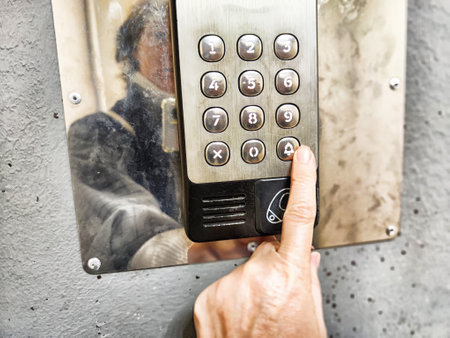 A person is pressing a button on a metal entry system outside a contemporary building while sunlight reflects on the surface.の写真素材