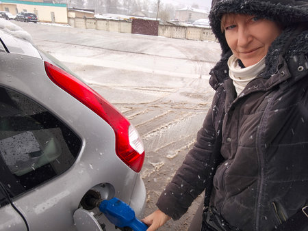 A middle-aged woman takes a selfie while refueling her car on a snowy day, highlighting her adventurous spirit in travel.の写真素材