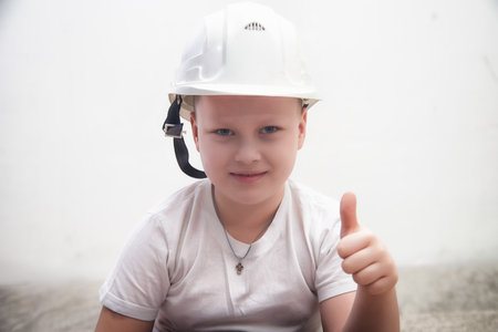 Young boy in construction helmet gives a thumbs up with confidence in a bright indoor settingの写真素材