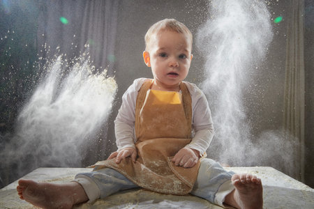A young boy joyfully plays with flour during a creative cooking-themed photo shoot in a studio...