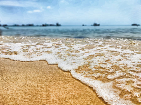 Crystal clear waves gently break on the golden sand of a serene beach, with distant boats dotting the horizon under a blue sky.の写真素材