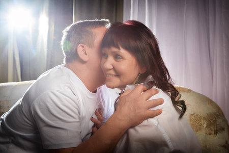 Middle-aged couple shares a tender moment during an intimate indoor photo shoot at their cozy homeの写真素材
