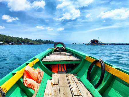 A colorful boat floats on turquoise water, with a view of an island and a distant village under a bright blue sky with clouds.の写真素材