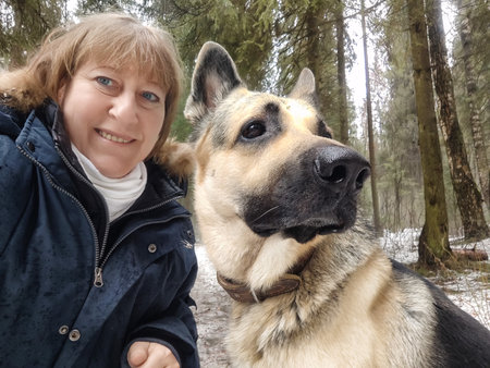 A woman smiles while taking a selfie with her dog in a lush, rain-soaked forest surrounded by tall trees.の写真素材