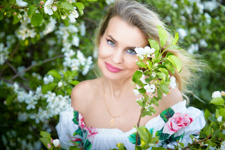 Mature blonde blogger posing with white flowers in a lush outdoor setting during soft daylight