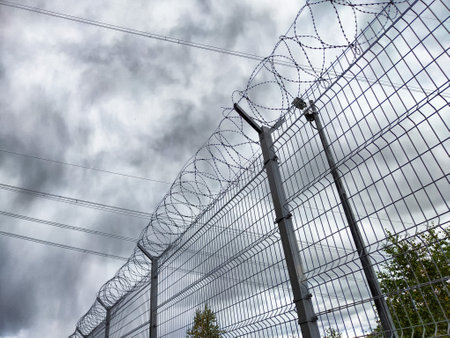 A high-security fence encircles the Krasnoyarsk Hydroelectric Power Station, stark against dark, stormy clouds above.の写真素材