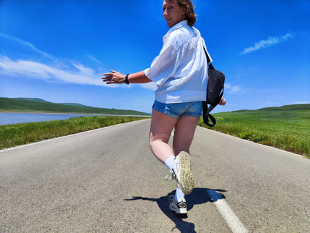 Blonde woman takes a joyful selfie while exploring a beautiful landscape on a sunny day with clear skies and vibrant greenery.の写真素材