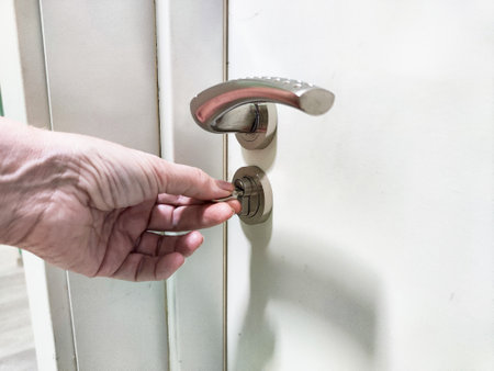 A hand is placing a key into the lock of a door, illustrating the action of unlocking a home entryway during a typical day.の写真素材