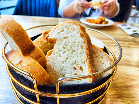 A basket filled with slices of freshly baked bread sits on a wooden table, while a diner enjoys a meal in the background.の写真素材