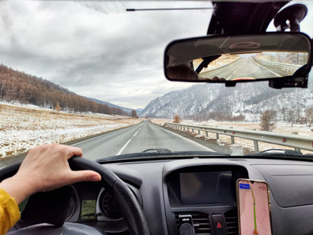 A woman drives on a snowy road surrounded by mountains, embracing the freedom of her winter adventure in nature's beauty.の写真素材