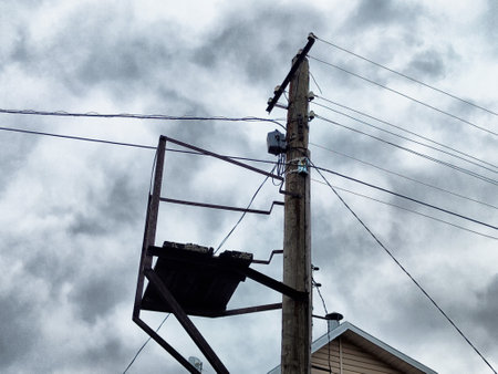 A utility pole stands tall, supporting multiple electrical wires, surrounded by overcast skies in a city area.の写真素材