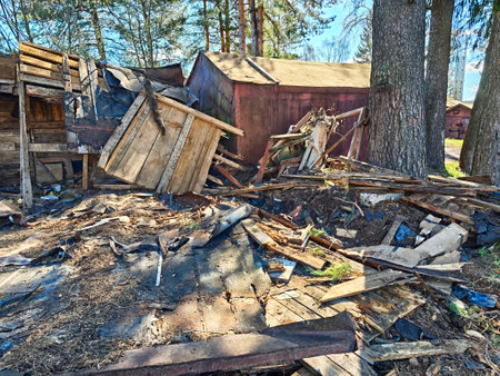 Abandoned wooden frameworks lie in disarray amidst piles of rubble and litter in a forested environment under clear blue skies.の写真素材
