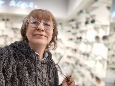 Woman with blonde hair tries on stylish glasses in an optics store, capturing a joyful moment in her daily life.の写真素材