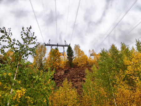 Krasnoyarsk Hydroelectric Power Station features high-voltage power lines against a backdrop of colorful autumn trees under a gray sky.の写真素材