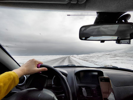 Snow blankets the landscape as a vehicle navigates an icy road during a blizzard. Dark clouds hang overhead, creating a dramatic winter atmosphere.の写真素材