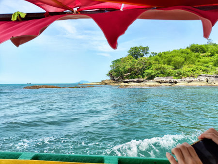 Enjoying a refreshing boat ride across clear waters, surrounded by greenery and rocky formations on a bright day.の写真素材