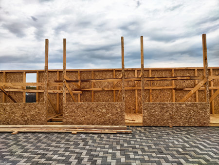 Wooden framing is being erected at a construction site, showcasing a skeletal structure against a cloudy sky, indicating progress.の写真素材