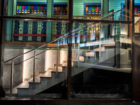 A beautifully lit staircase with sleek railings is visible through large glass windows, showing vibrant colored glass panels above.の写真素材