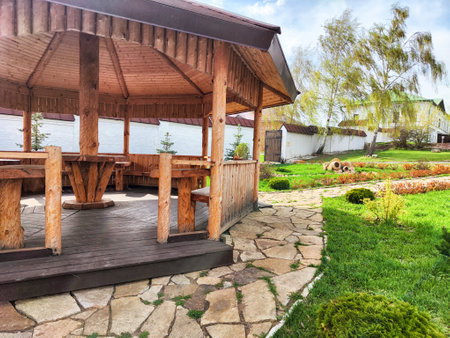 Wooden gazebo offers shade and seating beside a tranquil lake, framed by manicured grass and a stone walkway on a clear day.の写真素材