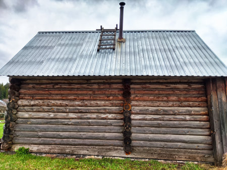 Weathered wooden cabin stands proudly with a metal roof in a peaceful mountain setting under gray skies, showcasing rustic charm.の写真素材