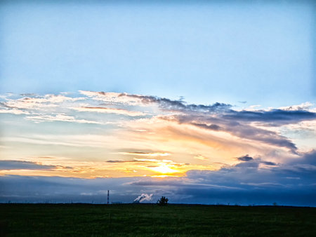 A breathtaking sunset unfolds with vivid colors reflecting on the clouds, creating a calming atmosphere across the open landscape.の写真素材