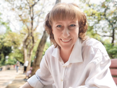 Mature woman smiles for a selfie in a lush, green park, capturing a moment of her travel adventure and lifestyle blogging.の写真素材