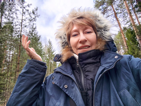 Blonde woman enjoying a winter adventure outdoors, capturing a moment with a cheerful smile in a beautiful forest landscape.の写真素材