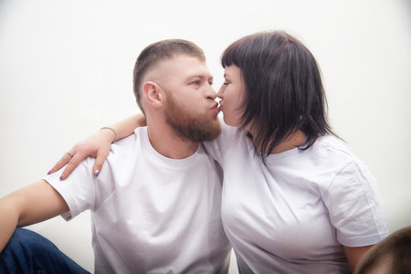Couple sharing a tender moment while sitting closely together in casual attire against a minimalist backgroundの写真素材