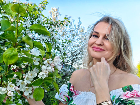 Mature blonde woman posing outdoors with flowers in spring, capturing a joyful lifestyle momentの写真素材