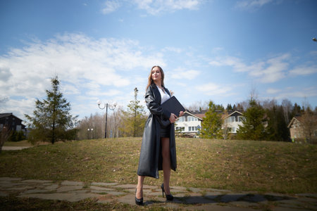 Confident woman in stylish outfit holding a folder outside modern houses on a sunny dayの写真素材