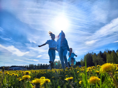 Children play joyfully in a sunny dandelion field during late spring in a rural landscapeの写真素材