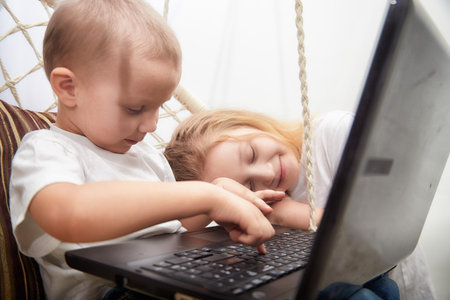 Children enjoying a playful moment while using a laptop in a cozy indoor setting