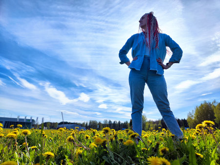 A person stands confidently among vibrant dandelions under a blue sky in a serene field during daylight hoursの写真素材