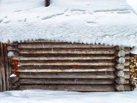 A cozy log cabin stands surrounded by a blanket of snow, with logs peeking through the winter scene.の写真素材