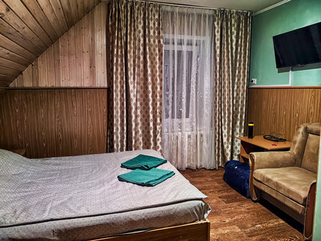 This bedroom cozy features a neatly made bed with green towels, a comfortable armchair, and soft evening light streaming through the curtains.の写真素材