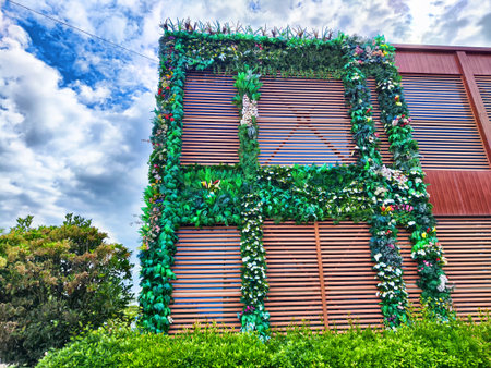 A vibrant vertical garden covers a contemporary building, showcasing a variety of plants and flowers against a cloudy sky.の写真素材