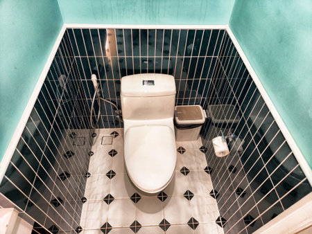 A small yet modern restroom showcases a sleek toilet setup against vibrant green tiles and elegant patterned flooring, creating a unique ambiance.の写真素材
