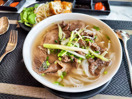 Hot bowl of Vietnamese pho features thinly sliced beef, fresh herbs, and rice noodles, enjoyed in a...