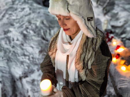 Middle-aged woman enjoys a humorous winter night walk in the snowy forest holding a candleの写真素材