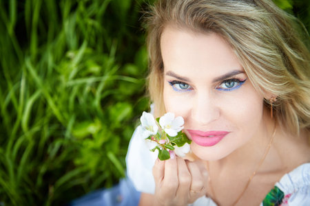 Blonde woman posing with flowers in a lush green setting during a bright daylight momentの写真素材