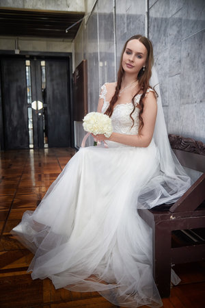 Elegant bride in a wedding dress poses with bouquet before ceremony in a charming venue settingの写真素材