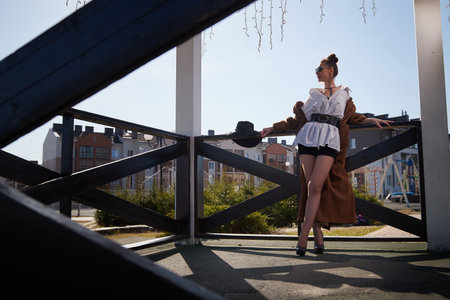 Woman in stylish outfit poses confidently in urban park during sunny dayの写真素材
