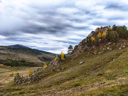 Colorful autumn trees crown rocky hills above a serene valley, highlighting the mountain landscape beauty on an overcast day.の写真素材