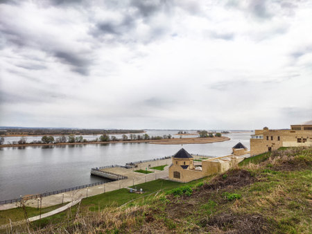 Cloudy day overlooking a wide river with green grass and historical structures lining the bank, showing casing nature and architecture.の写真素材