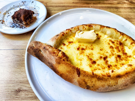 A warm cheese bread topped with butter is served alongside a small dessert at a casual dining place during midday.の写真素材
