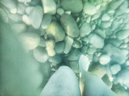 Feet standing in clear water over smooth stones, capturing a peaceful moment of connection with nature in a serene aquatic environment.の写真素材