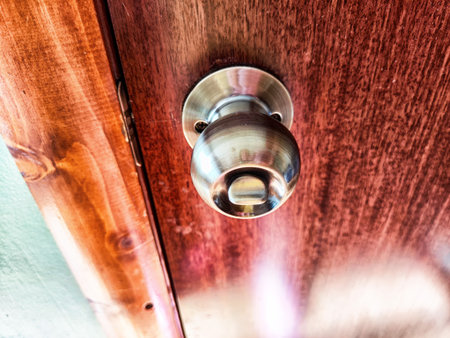 The image features a modern metallic door knob on a rustic wooden door, showing the contrast between sleek and textured materials.の写真素材